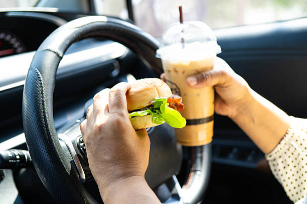 Asian woman driver hold and eat hamburger and cold coffee in car.